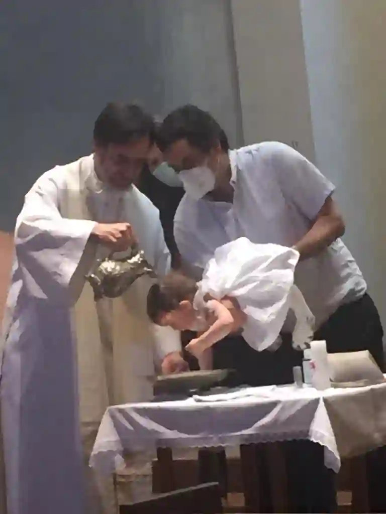 ceremonia de bautizmo en iglesia, justo en el momento que el cura vierte agua bendita sobre la cabeza del bebé, el papá la sostiene