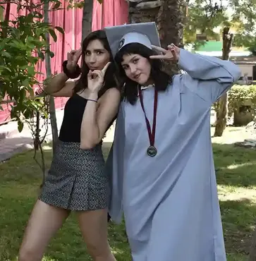Foto de alumna con toga gris y su amiga posando con libertad
